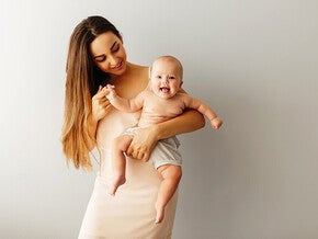 Photograph: smiling woman holding laughing baby against neutral background