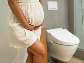Photograph: pregnant woman standing by toilet, hand on belly in modern bathroom