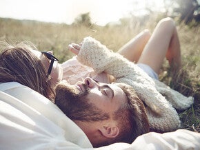 Photograph of a relaxed couple lying in sunlit grass, bearded man and woman with sunglasses