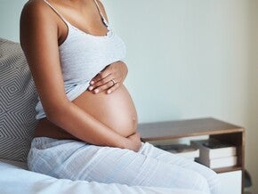 Бременна жена, седяща на легло, докосва корема си.