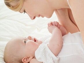 Фотография: усмихната майка гледа бебе на бял чаршаф