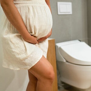 Photograph: pregnant woman standing by toilet, hand on belly in modern bathroom