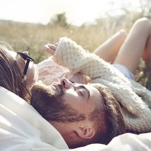 Photograph of a relaxed couple lying in sunlit grass, bearded man and woman with sunglasses