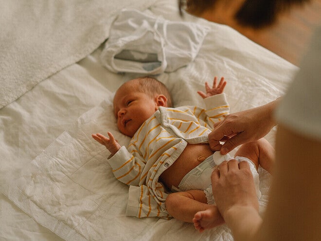Photograph of newborn on white sheet in striped outfit, adult hands adjusting diaper