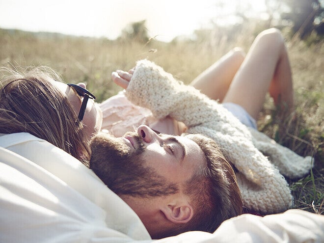 Photograph of a relaxed couple lying in sunlit grass, bearded man and woman with sunglasses