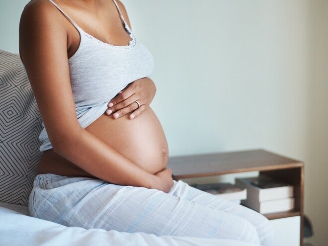 Бременна жена, седяща на легло, докосва корема си.