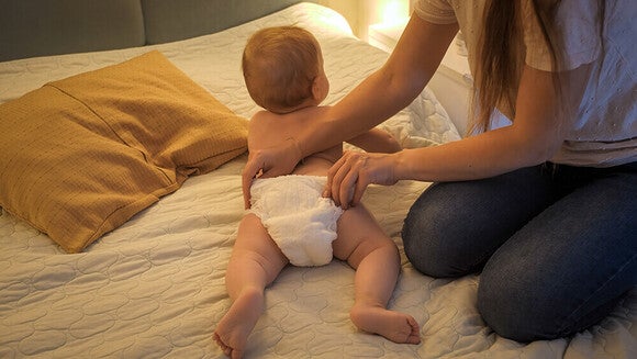 Photograph: baby on stomach as caregiver adjusts diaper on bed