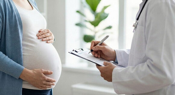Pregnant woman holding her belly as a doctor with stethoscope writes on a clipboard