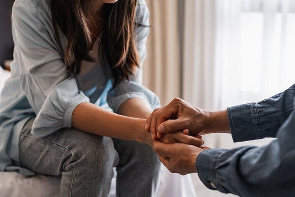 Photo: woman and older person clasping hands on couch, comforting moment